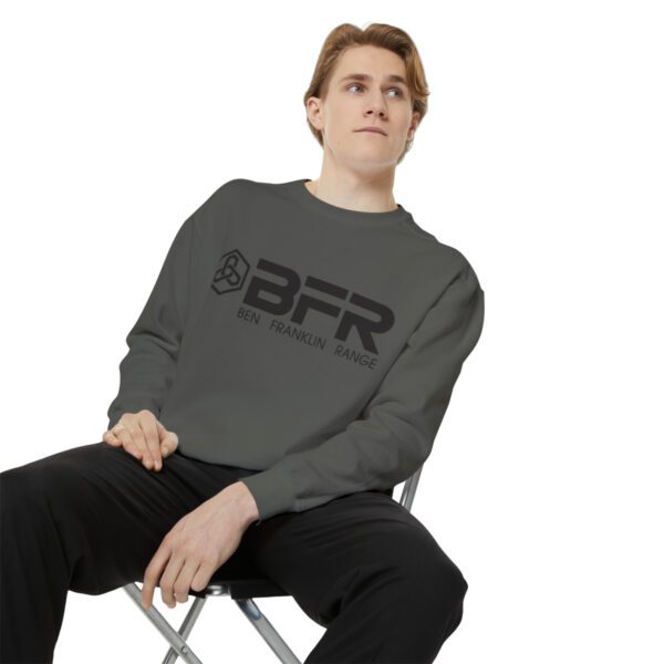 A man sitting on a chair wearing a BFR Logo - Unisex Garment-Dyed Sweatshirt.